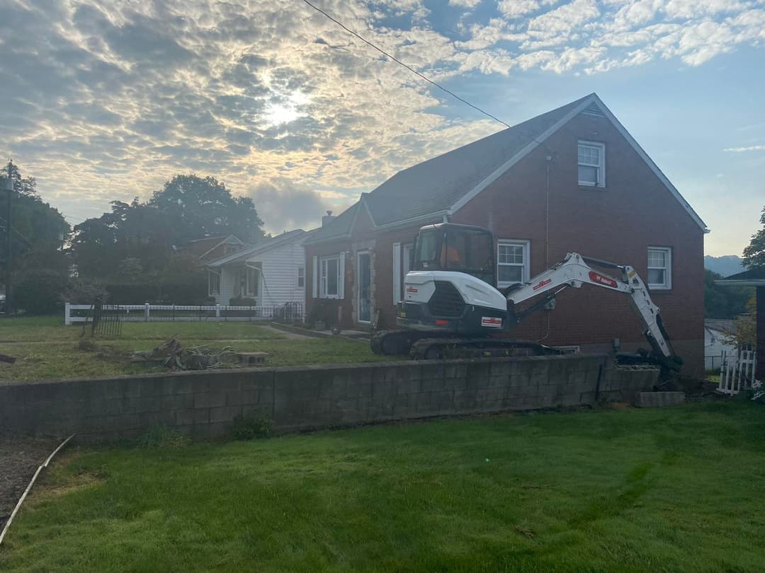 Excavator working near a house under a cloudy sky, showcasing landscaping project.
