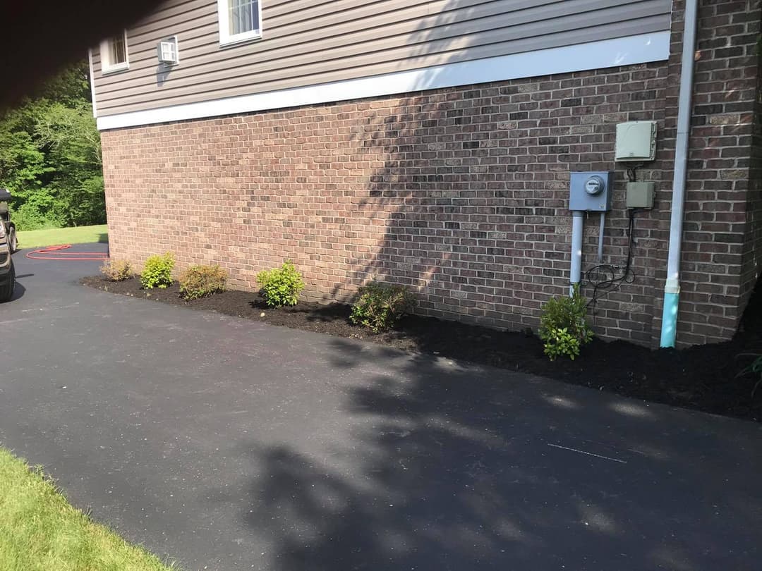 Well-maintained driveway with landscaped planting beds alongside a brick house exterior.