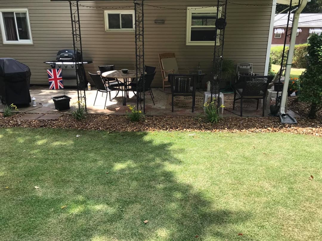 Patio area with seating, grill, and British flag, surrounded by landscaped lawn and garden.