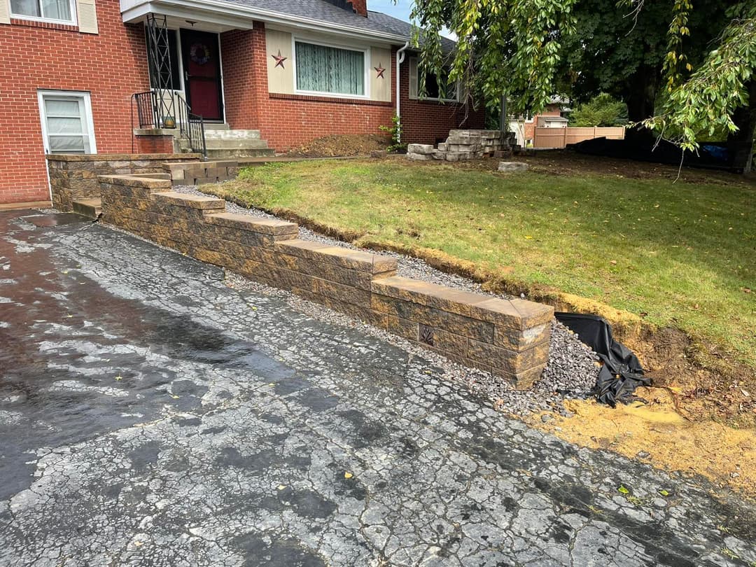 Newly constructed stone retaining wall and landscaped yard next to a red brick house.