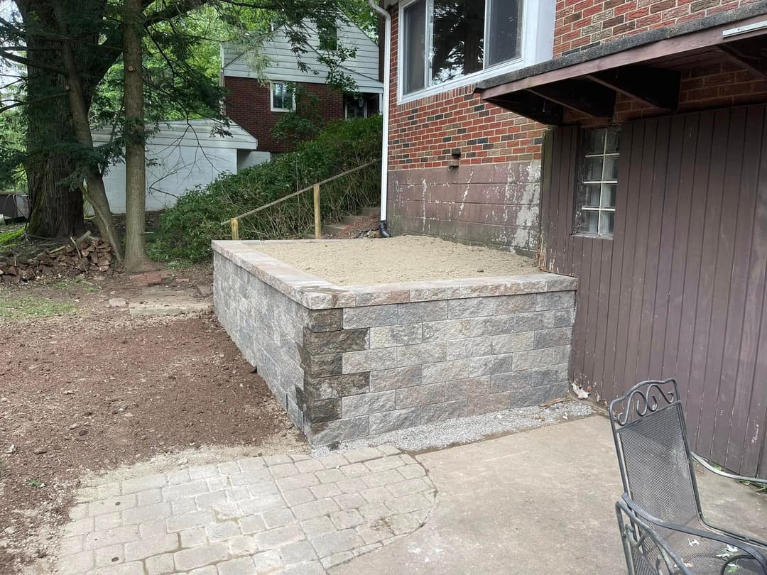Landscaped patio area with stone retaining wall and sand base near brick house.